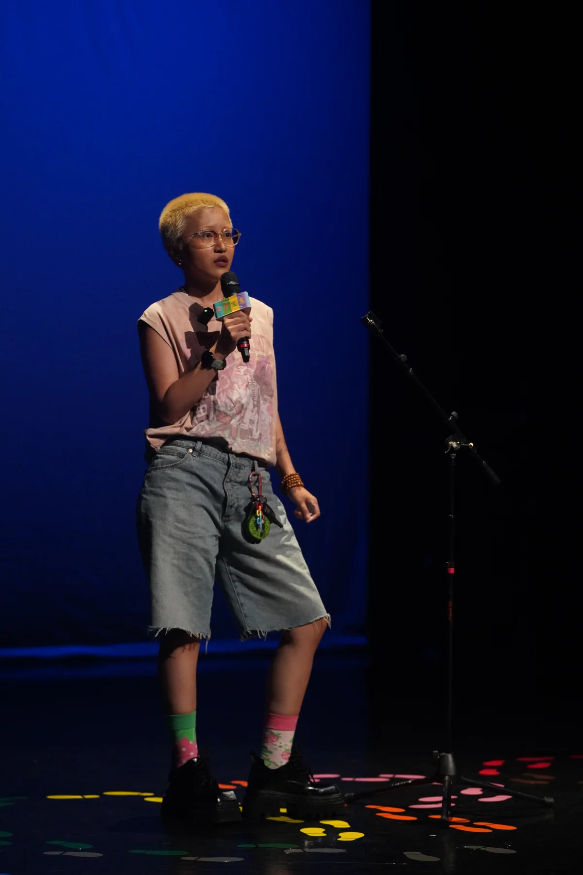 Raw ABEI holding a microphone, shown full-length on a blue-lit stage